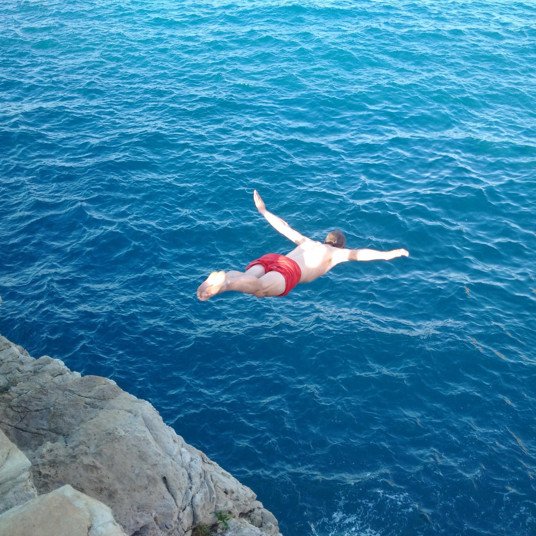 Klaas Joosten diving head-first off a limestone cliff into deep blue sea, arms spread wide.